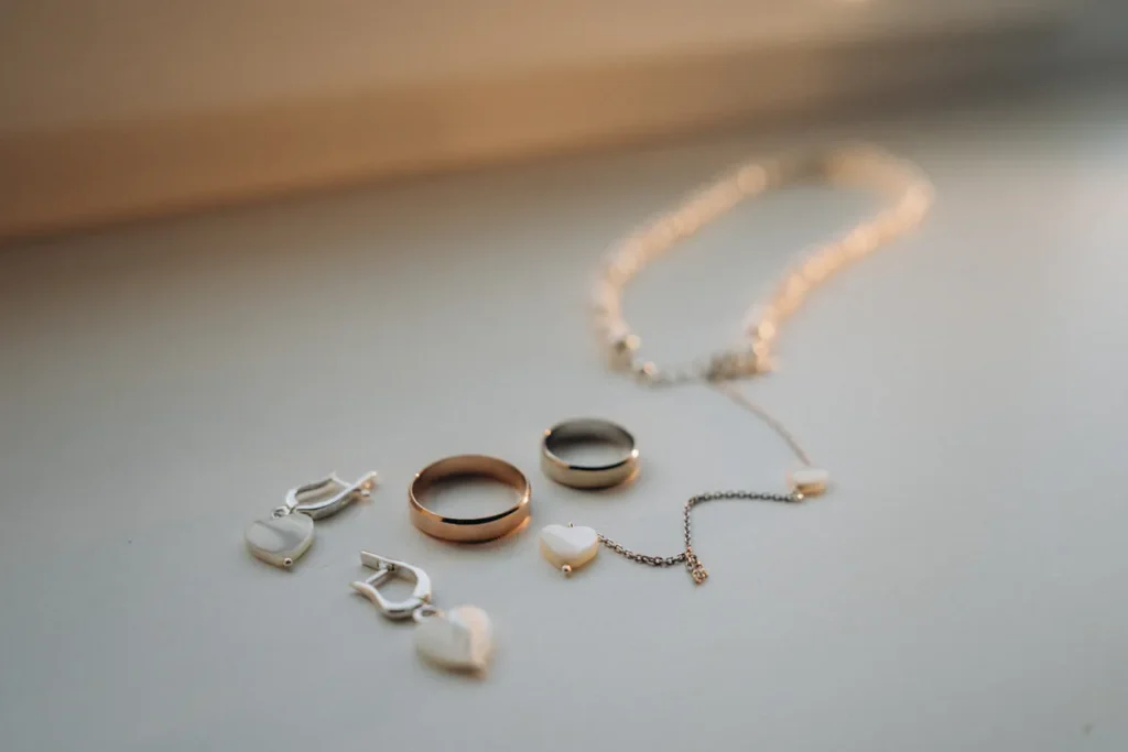 Deux alliances dorées, un bracelet de perles, un collier à pendentif cœur et des boucles d'oreilles cœur nacrées posés sur une surface claire