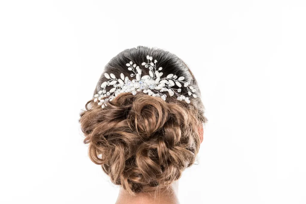 Chignon de mariée bouclé vu de dos, orné d'un peigne à fleurs et perles argentées, sur fond blanc