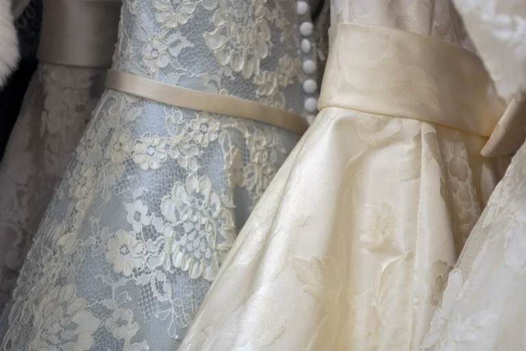 Gros plan sur des robes de mariée en dentelle ivoire et bleu pâle, ceintures en satin et boutons recouverts