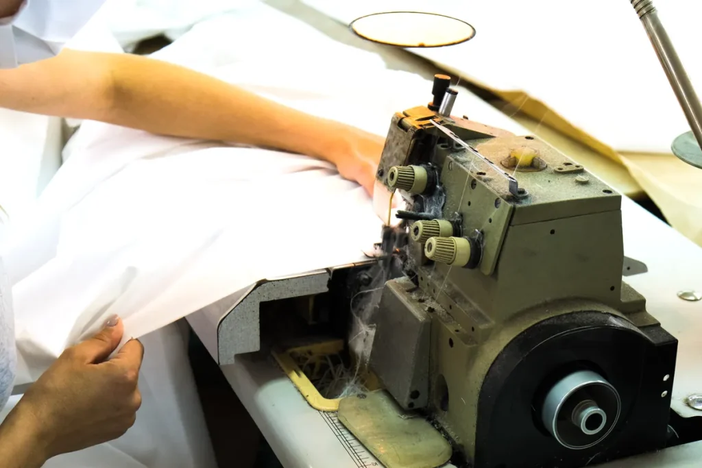 Mains d'une couturière guidant un grand tissu blanc dans une surjeteuse industrielle en plein travail